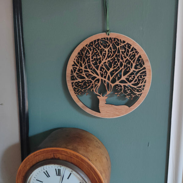 Wooden wall ornament hanging above a clock of a stag with antlers that create branches of a tree