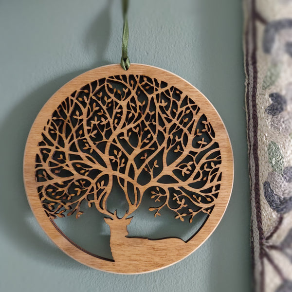 Wooden wall ornament hanging next to a curtain of a stag with antlers that create branches of a tree